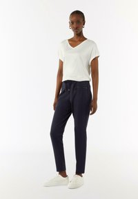Witte v-hals t-shirt gecombineerd met marineblauwe joggerbroeken met ritszakken en een touwtjesluiting. Draagt het met witte sneakers.