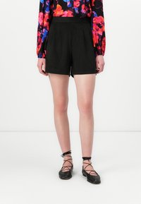 Sorte shorts med en skreddersydd passform, glatt stoff, midje i middels høyde og minimal detaljer, sammen med svarte snørestøvletter.