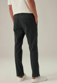 Schwarze, leichte Hose mit lockerer Passform, elastischem Bund und Gesäßtaschen, kombiniert mit weißen Turnschuhen vor einem neutralen Hintergrund.