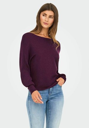 Lila gerippter Pullover mit einem Bootsausschnitt und langen Ärmeln, kombiniert mit hellblauen Jeans. Weiche Textur und lässige Passform.