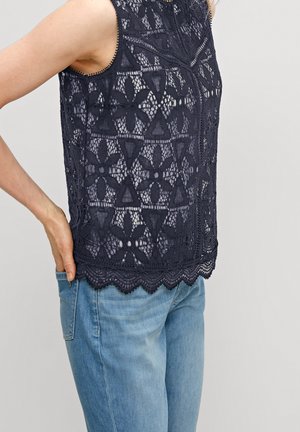Marineblauwe kanten top met bloemenpatronen, een gegolfde zoom, mouwloos ontwerp en ingewikkelde textuur, gecombineerd met lichtblauwe jeans.