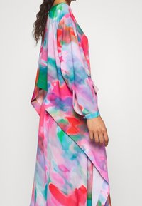 Un vestido largo y fluido que presenta un patrón abstracto multicolor en tonos de rosa, verde y azul. Está hecho de una tela ligera y aireada con mangas sueltas.
