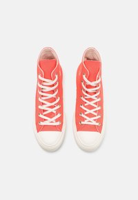 Zapatillas altas de lona en un brillante color coral con cordones blancos y puntera de goma. Presentan ojales metálicos y un interior acolchado de color rosa.