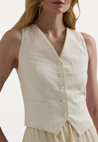 Colete texturizado creme, com decote em V, cinco botões e dois bolsos de pate; tecido liso com um padrão listrado subtil.