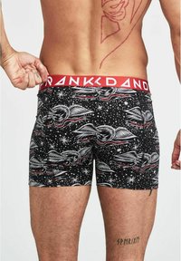 Svarta boxershorts med vingdesign i vitt och rött, med en röd midjeband med texten "FRANK DANDY". Mjuk, elastisk material.