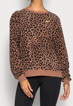 Bruine sweatshirt met luipaardprint, lange mouwen en klein geel Nike-logo op de borst, gedragen met een zwarte broek.