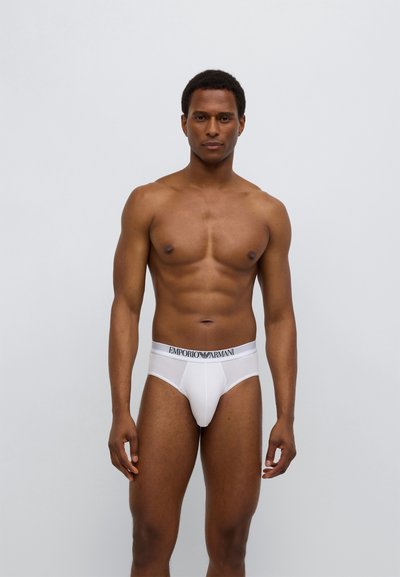 Λευκά βαμβακερά εσώρουχα με ζώνη μέσης με λογότυπο, με εφαρμοστή σχεδίαση και λεία υφή, εμφανίζονται σε ουδέτερο φόντο.