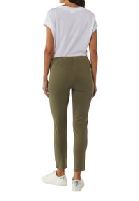 Olijfgroene tapered pantalons met een elastische tailleband, gecombineerd met een witte shirt met korte mouwen en witte sneakers met zilveren accenten.