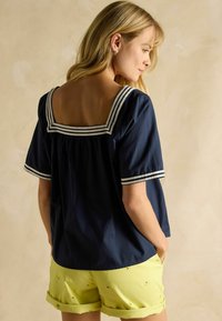 Bluza albastru închis cu decolteu pătrat, margini cu dungi și mâneci scurte, asortată cu pantaloni scurți galben deschis cu modele de lămâi.