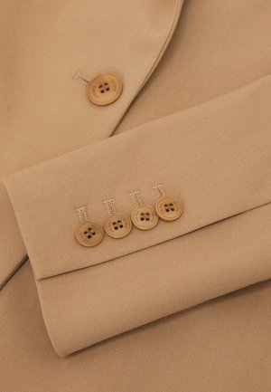 Tissu de veste beige clair avec une texture lisse, présentant quatre boutons marron sur la manche et un bouton supplémentaire au col.