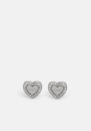 Zilveren hartvormige studs met in het midden de gegraveerde merknaam, omringd door kleine heldere edelstenen.