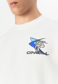 Primo piano di una persona che indossa una maglietta bianca con una grafica blu di un surfista e il testo "O'NEILL" sul petto.