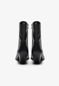 Botas de tobillo de cuero negro con un acabado texturizado, cierre de cremallera y tacón bajo cuadrado. Los remaches decorativos a lo largo del costado realzan el diseño.