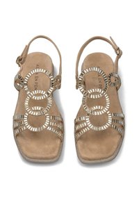 Sandales à talon en suede beige avec des accents métalliques circulaires et des lanières horizontales. Design à bout carré et boucle de cheville réglable.