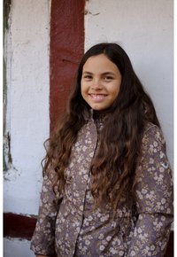 Chaqueta marrón con estampado floral y capucha, con flores de colores claros y una cinturilla elástica. La tela parece suave y ligera.