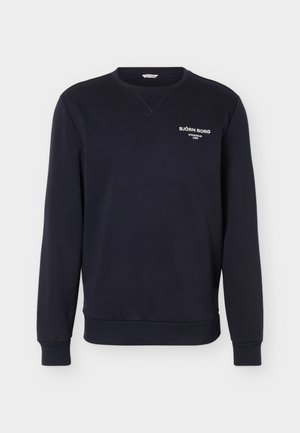 Tmavě modrá mikina s dlouhým rukávem a kulatým výstřihem, s bílým nápisem "Björn Borg Stockholm 1956" na levé straně hrudi a žebrovanými manžetami a lemem.