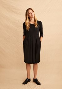 Abito nero al ginocchio con maniche a tre quarti, caratterizzato da tasche laterali e gonna plissettata, realizzato in un tessuto morbido e liscio.