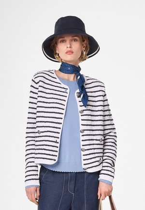 Wit en marineblauwe gestreepte cardigan van textuurstof, met ronde halslijn, zilveren knopen, gecombineerd met een lichtblauw topje en een marineblauwe bucket hat.