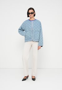 Μπλε καπιτονέ μπουφάν με διακοσμητικό μοτίβο ρόμβου, στρογγυλό ντεκολτέ, κουμπιά μπροστά και δύο πλαϊνές τσέπες, σε συνδυασμό με παντελόνι εκρού και μαύρες ψηλοτάκουνες γόβες.