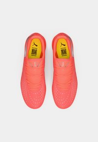 Lyse koralfarvede træningssko med en glat syntetisk overdel, der har ventilationshuller, fleksible snørebånd og en tekstureret sål for greb.