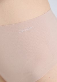 Calvin Klein naken sømløs undertøy med glatt tekstur, høy midjebånd og logo trykt på siden; minimalistisk design.