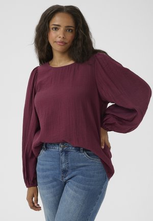 Burgundy long-sleeve top with texture, featuring a round neck and gathered sleeves. Paired with blue high-waisted jeans.