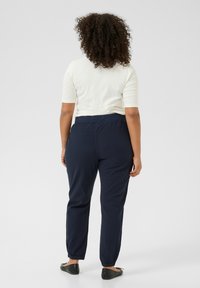Pantalones azul marino con una cinturilla elástica, piernas ajustadas y puños en los dobladillos. Combinados con una blusa blanca de manga corta y zapatos planos negros.