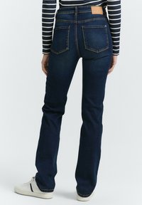 Jean en denim bleu foncé avec une coupe droite, deux poches arrière et une étiquette en cuir à la taille. Tissu texturé avec un léger stretch.
