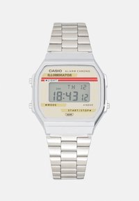 Montre numérique en acier inoxydable argenté avec un cadran rectangulaire, fond beige, accents rouges et jaunes, affichant l'heure et la date.