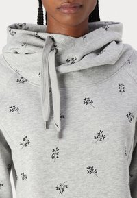 Szara bluza z kapturem typu golf, czarne wzory liści oraz sznurek ze stalowymi zakończeniami. Materiał ma miękką, teksturowaną powierzchnię.