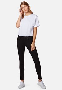 Camiseta blanca de algodón con mangas enrolladas, combinada con jeans skiny negros. Zapatillas blancas completan el conjunto. Diseño simple y casual.