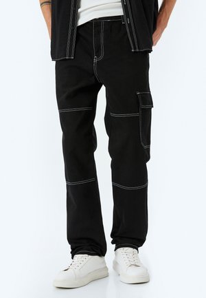 Sorte cargo-bukser med kontrasterende hvid stikning, der har sidelommer, en afslappet pasform og et holdbart stof. Hvide sneakers fuldender looket.