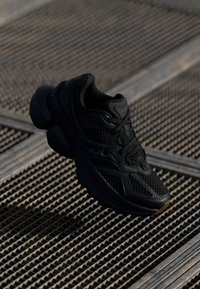 Sneakers sportivi neri in materiale mesh e sintetico, con una suola in gomma spessa, motivi intricati e chiusura a lacci.