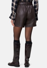 Brune faux læder shorts med elastisk talje og bælte. Båret over gennemsigtige sorte strømpebukser med knæhøje glansfulde burgunder støvler.