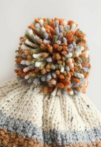 Strickmütze in Creme mit blauen und orangefarbenen Akzenten; oben mit einem bunten, flauschigen Pom-Pom verziert, das Nuancen von Grün, Orange und Grau aufweist.