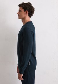 Marineblauwe gebreide trui met een gestructureerde afwerking, V-halsontwerp en geribde manchetten. Zijspleet met een merklabel aan de onderrand.