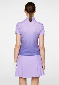 Lilla golf polo-shirt med korte ærmer og en lidt mørkere gradient i bunden, parret med en matchende plisseret nederdel. Overfladen er glat.
