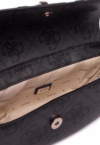 Interno di una borsa sintetica nera con finitura testurizzata, dotato di foderato beige, logo stampato e chiusura a scatto metallica.