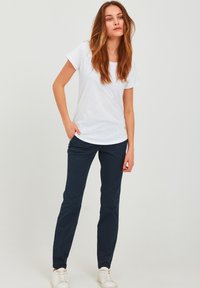 Hvit kortermet T-skjorte kombinert med marineblå slim-fit bukser og hvite joggesko, med et enkelt design og glatt tekstur.