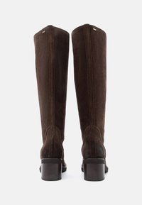 Botas de ante marrón hasta la rodilla con tacón cuadrado, que presentan costuras visibles y una textura suave. Diseño sencillo, sin acentos adicionales.