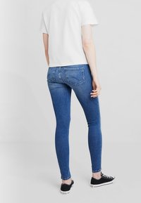 Jeans ajustados de mezclilla azul con cintura de altura media, con bolsillos traseros. Combinados con unas zapatillas negras y una camiseta blanca de manga corta.