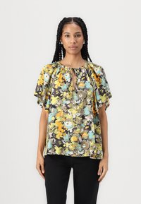 Blomstrete bluse i gule, grønne og oransje nyanser, med en nøkkelhullsutrigning og fløteermer. Laget av lettvektig stoff.