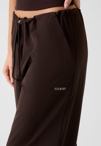 Bruine sportbroek met een elastische tailleband, zijzakken en een zilveren logo op de dij. Gemaakt van glad, lichtgewicht materiaal.
