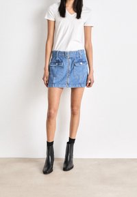 Jeansminikjol med två framfickor, en dragkedja och ett bälte. Ljusblå färg, rak form. Kombinerad med svarta anklarstövlar och en vit V-ringad topp.