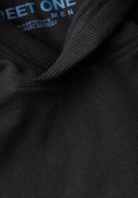 Svart bomullströja med ribbat rundhals. Har blå tryckt text inuti kragen som säger "STREET ONE MEN." Mjuk känsla.