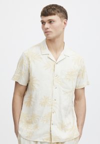Short-sleeve shirt in light beige linen with a palm tree pattern. Features a pocket, button front, and relaxed fit.
