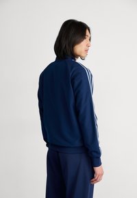 Kék síning kabát sima anyagból. Fehér csíkokkal díszítve a vállakon és az ujjakon, álló gallérral és rugalmas mandzsettákkal.