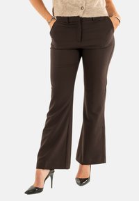 Pantaloni marroni, leggermente svasati, con tasche laterali, texture liscia e vestibilità su misura, abbinati a scarpe nere lucide con tacco alto.