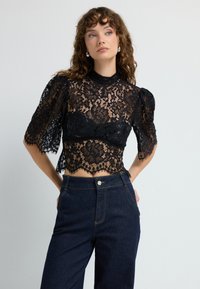 Sorte blonde cropped top med pufærmer og høj hals, prydet med blomster mønstre. Matchet med højtsiddende mørke denim bukser.