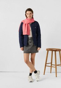 Giacca imbottita blu navy, sciarpa rosa chiaro, gonna di jeans grigia e sneakers argento con calzini neri. Design semplice, stile casual e tessuti testurizzati.